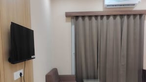 Habitación de hotel con cama, sofá, televisor montado en la pared, aire acondicionado y ventana con cortinas.