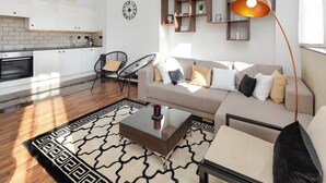 Ett modernt vardagsrum med en soffa, ett soffbord och stolar, ett kök i bakgrunden och en stor bokhylla.