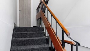 Eine Treppe mit hölzernem Geländer und schwarzen Metallspindeln, die zu einer Tür mit einem Lichtschalter darüber führt.