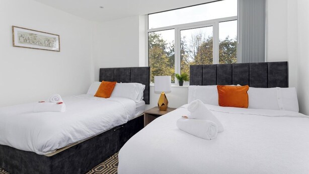 Ein Hotelzimmer mit zwei Betten, einem Fenster mit Blick auf Bäume und einem gerahmten Bild an der Wand.
