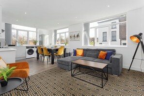 A modern living room with a grey sofa, a coffee table, and a patterned rug. - Flatzy - 16 Guests 4 En-suite Central Apartment B (Liverpool)