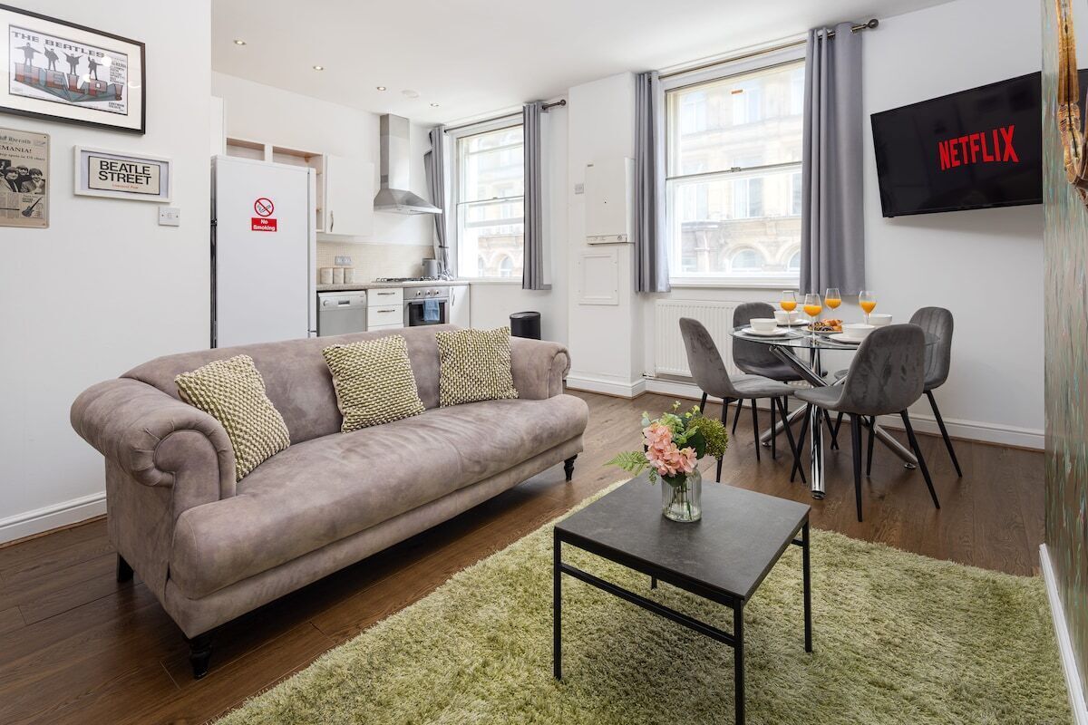 Una sala moderna con sofá, mesa de comedor con sillas, zona de cocina y televisor montado en la pared.