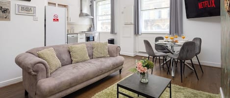 Una sala moderna con sofá, mesa de comedor con sillas, zona de cocina y televisor montado en la pared.