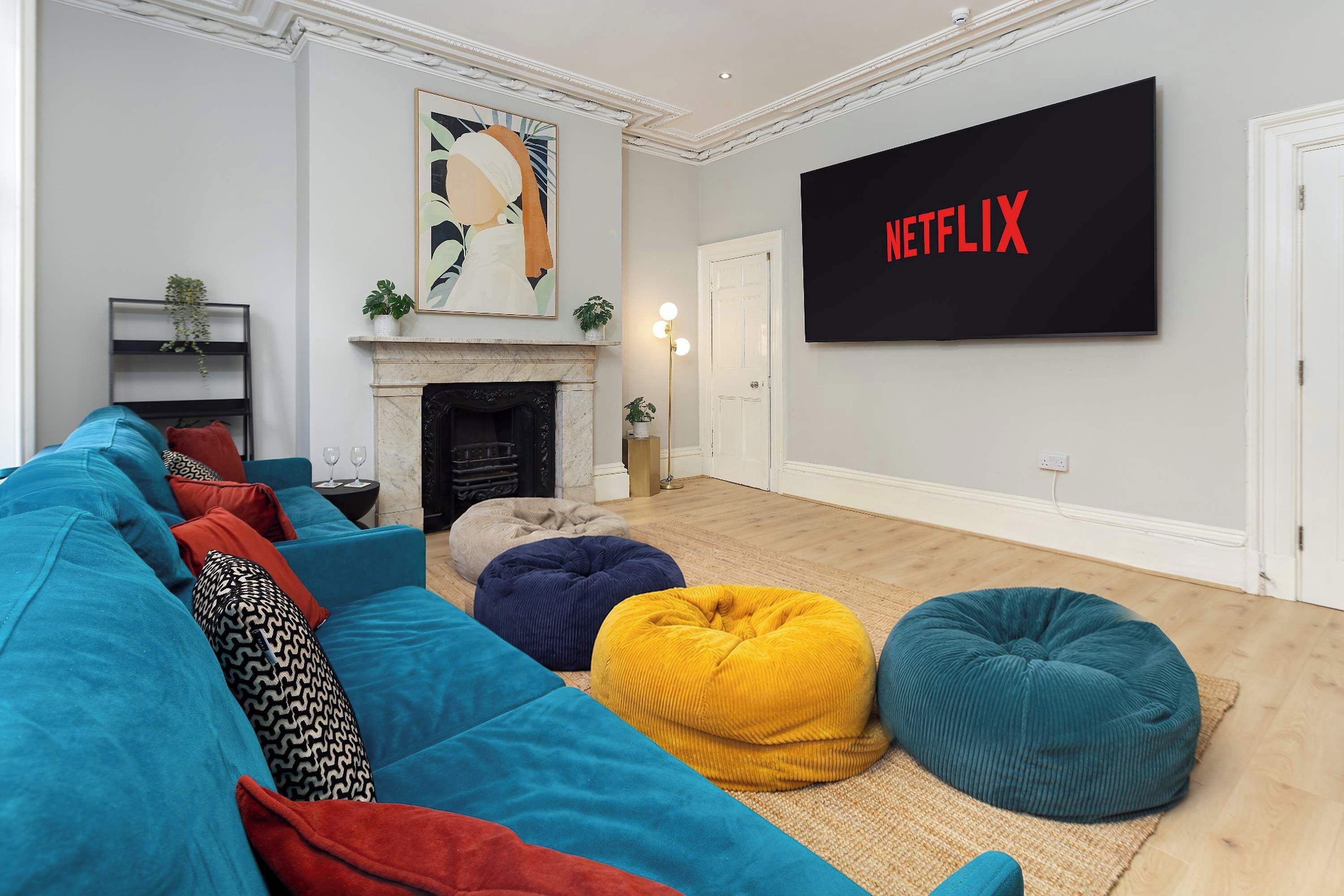 Ein Wohnzimmer mit einer Couch, bunten Sitzsäcken, einem Kamin und einem großen Fernseher, der 'NETFLIX' anzeigt.