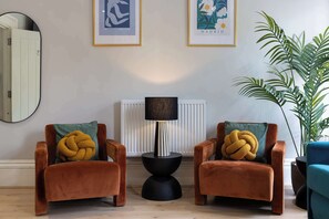 Un salon avec deux fauteuils marron, un lampadaire noir et une grande plante en pot.