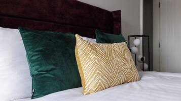 Ein Bett mit dunklem Kopfteil, weißer Bettwäsche und zwei Kissen, eines grün und eines gemustert.