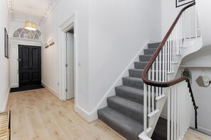 A staircase with a wooden handrail and white balusters, leading to a landing with a light fixture. - Flatzy - City Centre Mansion | Sleeps 22 | 5 Baths (Liverpool)