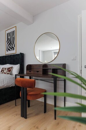 A bedroom with a bed, a desk with a chair, a round mirror, and a framed abstract artwork on the wall. - Flatzy - City Centre Mansion | Sleeps 22 | 5 Baths (Liverpool)