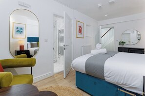 Une chambre à coucher moderne avec un lit, une chaise, un miroir rond et une porte donnant sur une salle de bain.