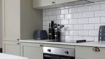 Een keuken met lichtgrijze kastjes, een witte betegelde achterwand, een ingebouwde oven en een aanrecht met een broodrooster en keukengerei.