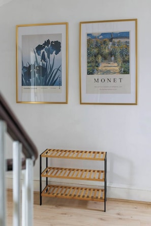 Zwei gerahmte Kunstwerke an einer Wand, darunter ein Holzregal.