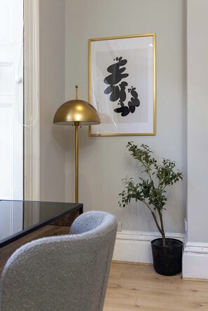 Une pièce comprenant un bureau, une lampe, une œuvre d’art encadrée et une plante en pot.