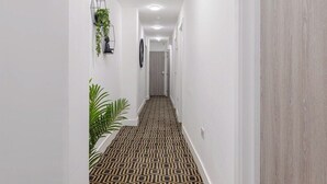 Ein Flur mit Teppichmuster, weißen Wänden und einer Holztür.