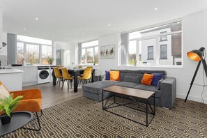 A modern living room with a grey sofa, a coffee table, and a patterned rug. - Flatzy - 16 Guests 4 En-suite Central Apartment A (Merseyside)