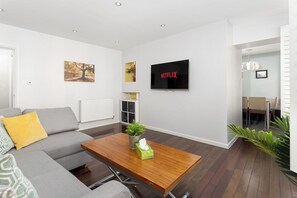 A modern living room with a grey sofa, wooden coffee table, and a flat-screen TV mounted on the wall. - Flatzy - 3 Bedroom Apt in Heart of City Centre (Liverpool)