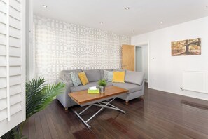 A modern living room with a grey sofa, wooden coffee table, and patterned wallpaper. - Flatzy - 3 Bedroom Apt in Heart of City Centre (Liverpool)