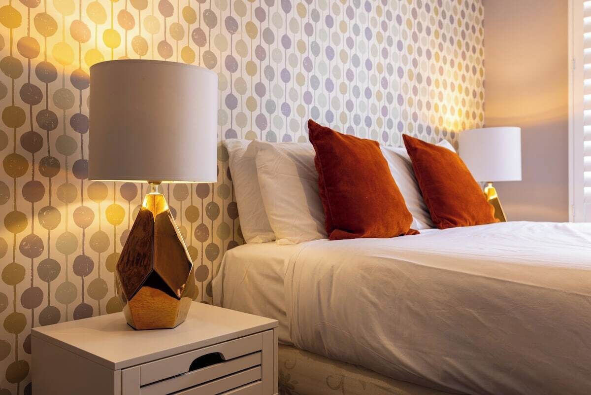 A hotel room with a bed, two nightstands, and a patterned wallpaper.