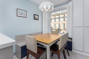 A dining area with a wooden table and chairs, a white pendant light, and a window with shutters. - Flatzy - 3 Bedroom Apt in Heart of City Centre (Liverpool)