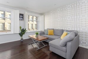 A modern living room with a grey sofa, wooden coffee table, and a potted plant. - Flatzy - 3 Bedroom Apt in Heart of City Centre (Liverpool)