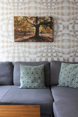 A grey sofa with patterned cushions against a wall with a geometric wallpaper. - Flatzy - 3 Bedroom Apt in Heart of City Centre (Liverpool)