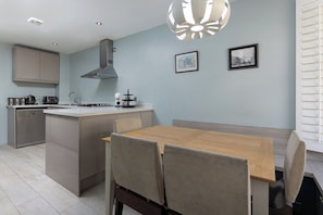 A modern kitchen with a central island, a dining table with chairs, and a pendant light. - Flatzy - 3 Bedroom Apt in Heart of City Centre (Liverpool)