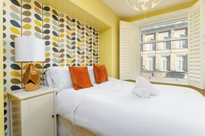 Une chambre d’hôtel avec un lit, une table de chevet, une lampe et une fenêtre avec des volets.