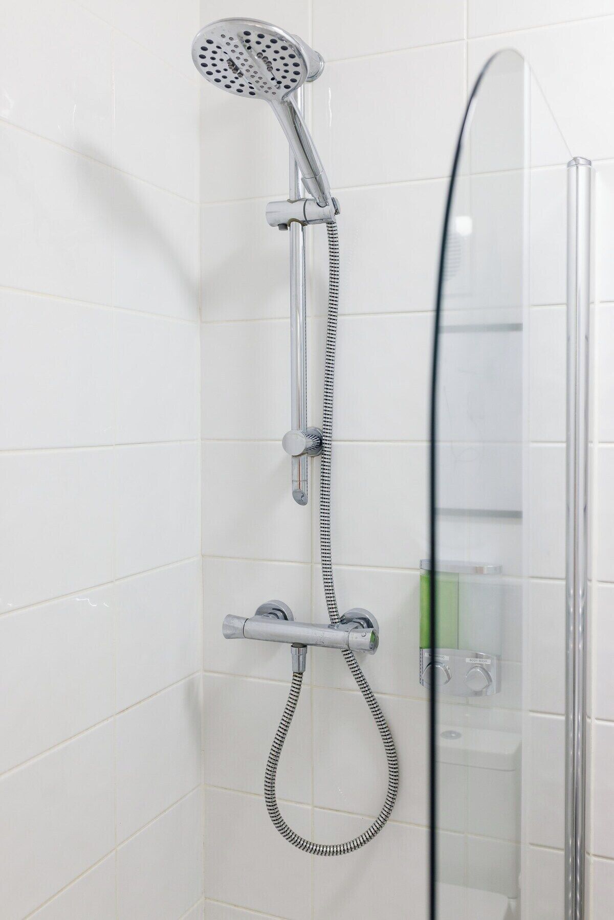A shower with a handheld showerhead, a wall-mounted control, and a flexible hose.
