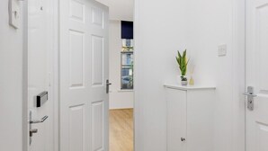 A hallway with white doors, a wooden floor, and a plant on a shelf. - Flatzy - Iconic Beatles and Liverpool Culture Home (Liverpool)