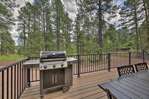 A deck with a portable grill, surrounded by a wooden deck and a metal railing, overlooking a forested area. - A-frame in the heart of Pinetop with AC (Pinetop-Lakeside)