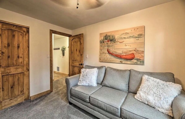 A living room with a grey sofa, two white fluffy cushions, and a painting of a canoe on a wooden background.