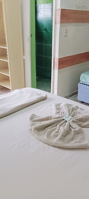 Una habitación con cama, toalla y zona de ducha con azulejos verdes.