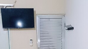 Une pièce comprenant un lit, un téléviseur fixé au mur, une fenêtre et une porte dotée d’un volet coulissant.