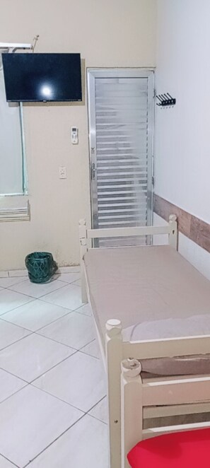 Una habitación con una cama, un televisor montado en la pared, una ventana y una puerta con persiana corredera.