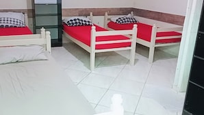 Une pièce comprenant trois lits en bois, chacun doté d’un matelas rouge et d’une tête de lit blanche, ainsi que d’un oreiller blanc orné d’un motif noir.