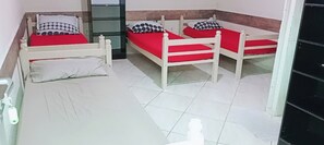 Una habitación con tres camas de madera, cada una con colchón rojo y cabecera blanca, y almohada blanca con diseño negro.