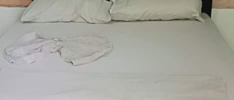 Una cama con una colcha blanca y almohadas, suelo de baldosas y pared verde.