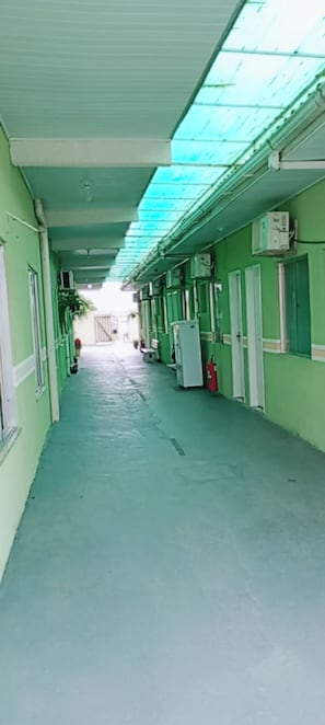 Corredor com portas em ambos os lados, piso ladrilhado e claraboia acima.