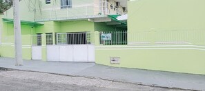 Edifício com entrada fechada por portão, varanda e placa indicando um negócio ou serviço.