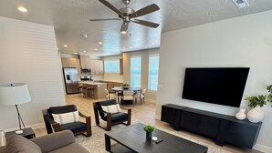 A modern living room with a sofa, coffee table, TV, and a dining area with chairs and a kitchen in the background.