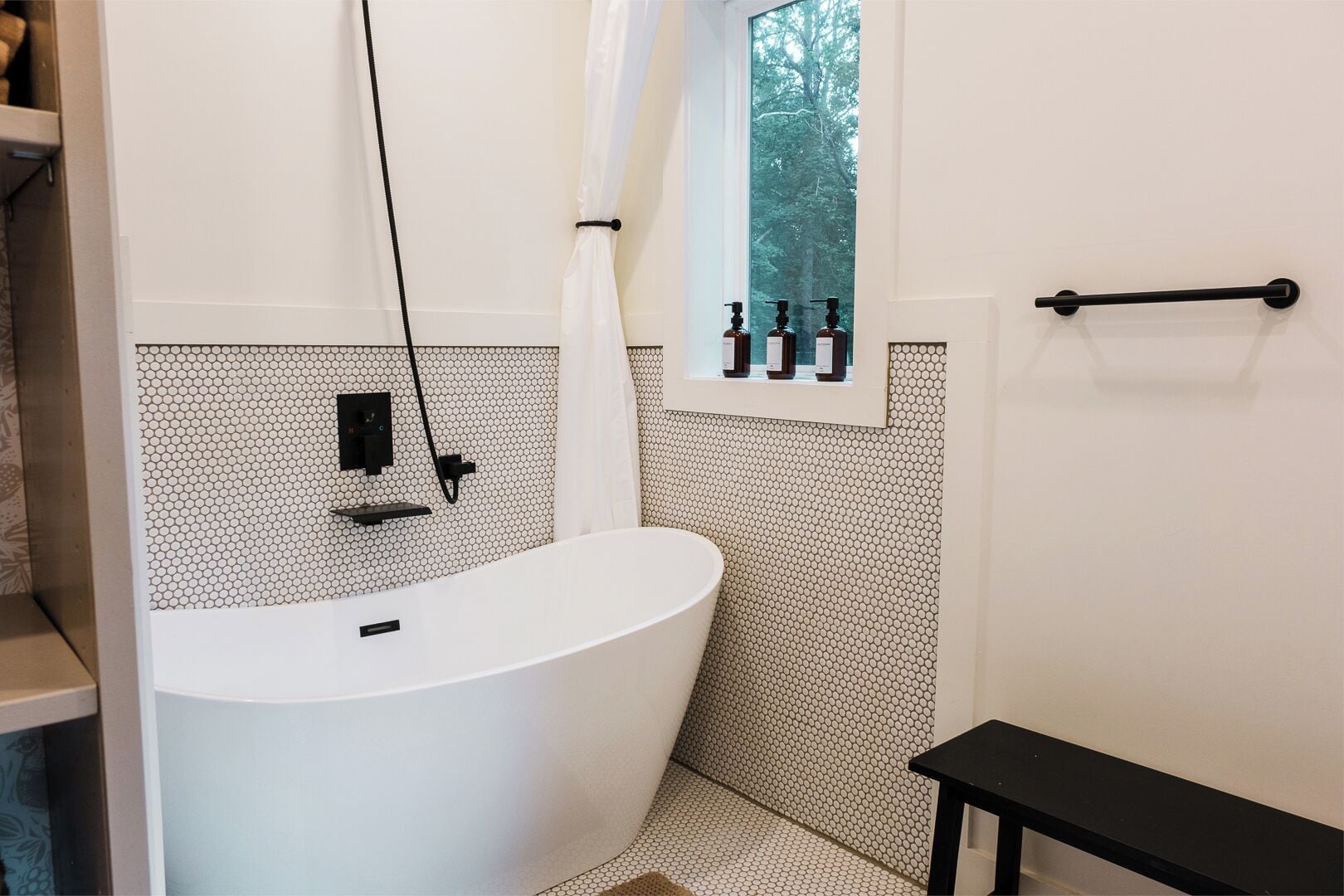 Un baño moderno con una bañera independiente, un ventanal con botellas y un perchero para toallas.