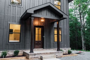 Une maison moderne à l’extérieur sombre, avec une porte d’entrée et un porche doté d’un luminaire.