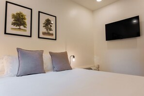 Une chambre d’hôtel avec un lit, deux oreillers, un téléviseur fixé au mur et deux tableaux représentant des arbres.