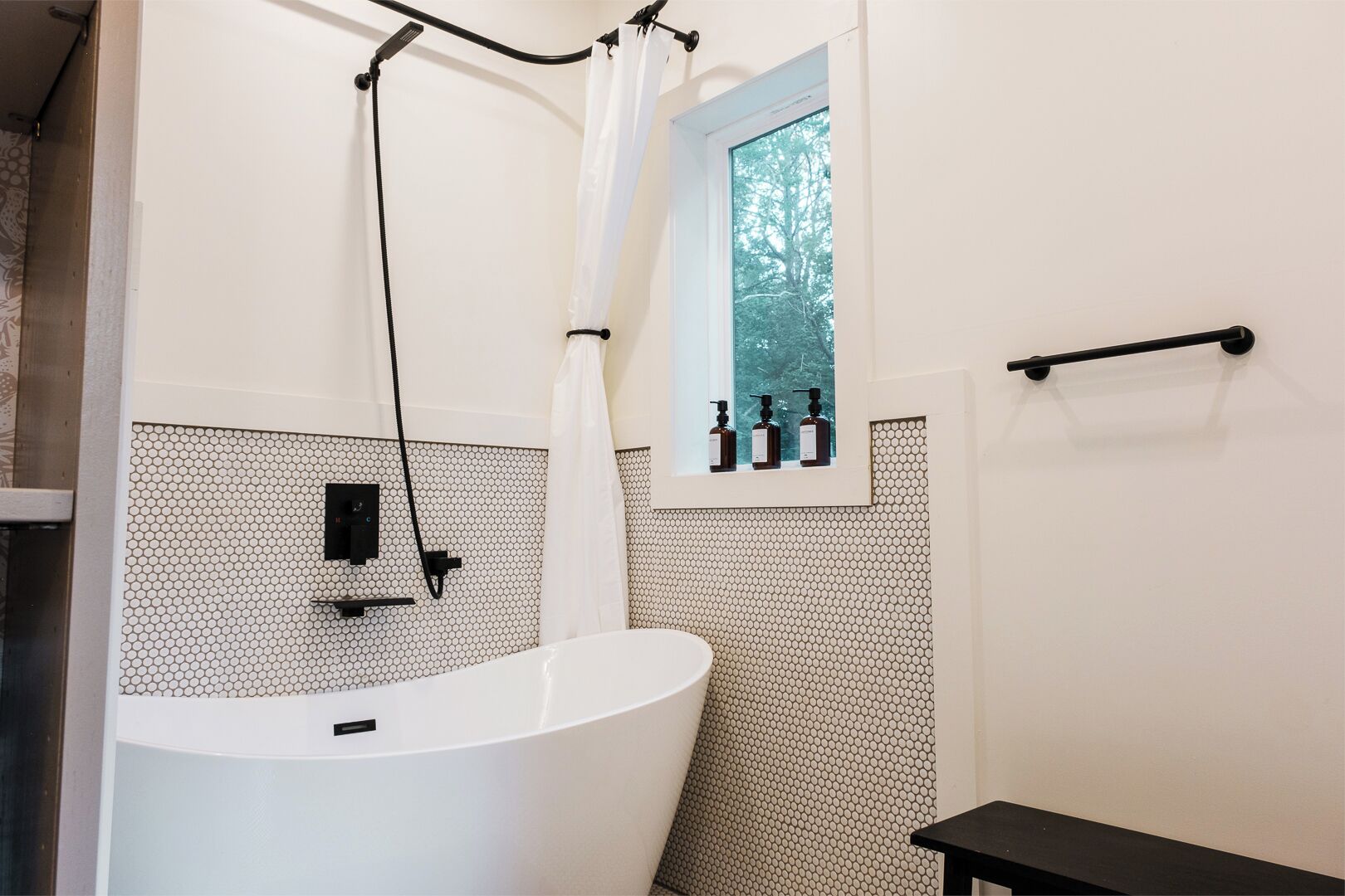 A bathroom with a freestanding bathtub, a window with a view of trees, and a towel rack.