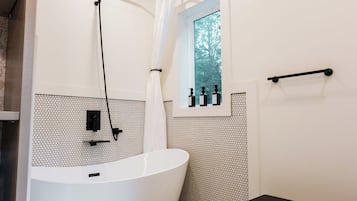 A bathroom with a freestanding bathtub, a window with a view of trees, and a towel rack.