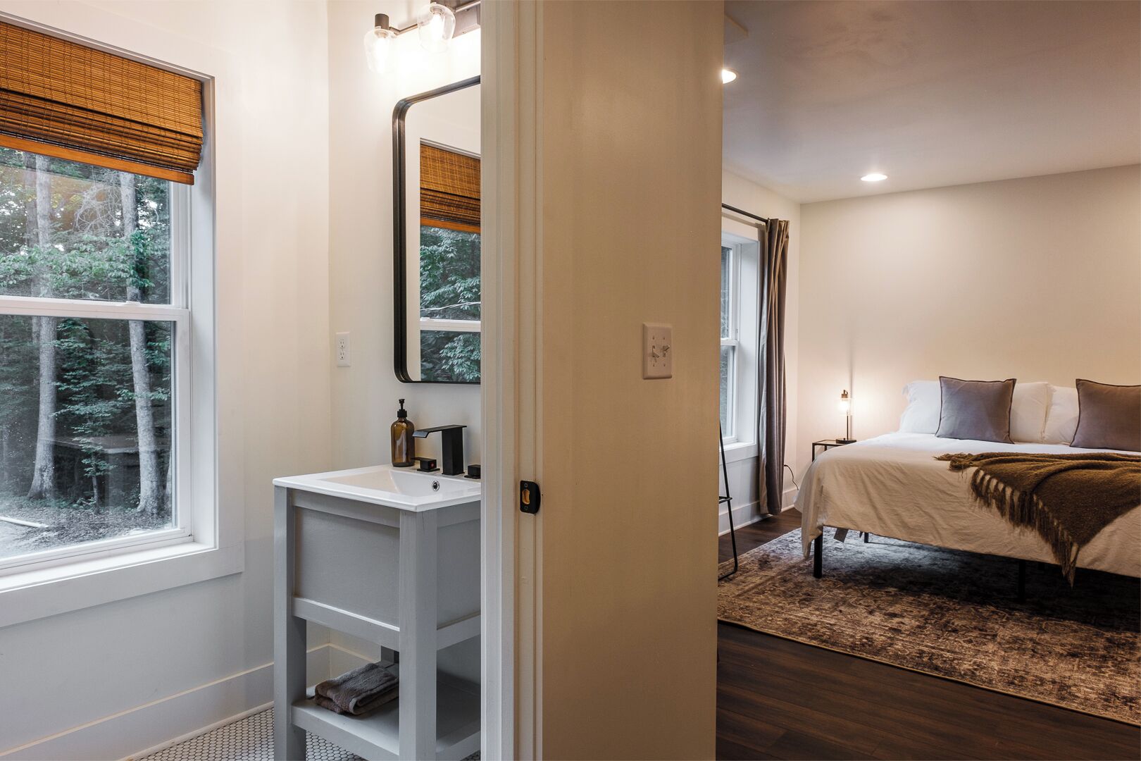 Een slaapkamer met een bed, nachtkastje en een raam met uitzicht op bomen.