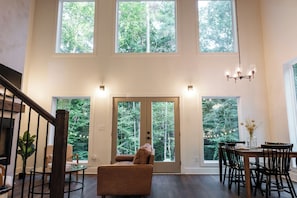 Un intérieur spacieux avec de hauts plafonds, de grandes fenêtres, un escalier, un coin repas et un espace salon.