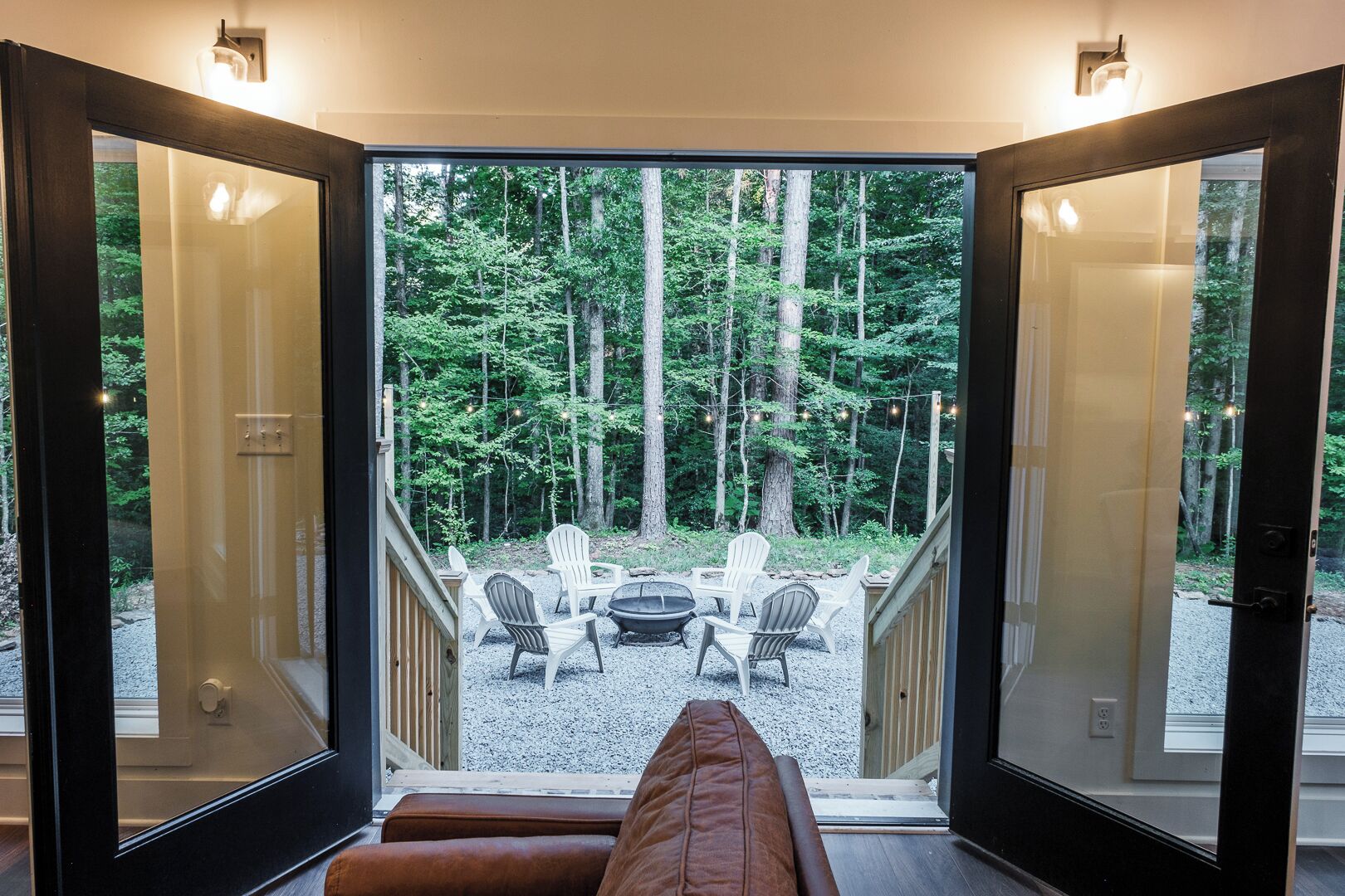 Une porte ouverte donnant sur une terrasse avec coin salon extérieur et vue sur la forêt.