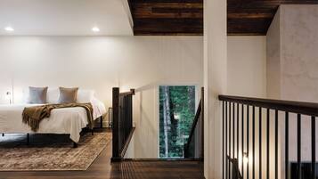 A bedroom with a large bed, a view of a forest through a glass door, and a wooden staircase.