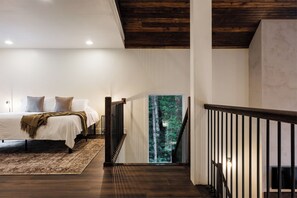 A bedroom with a large bed, a view of a forest through a glass door, and a wooden staircase.