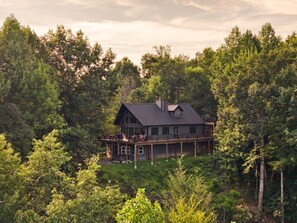 A two-story house with a deck, surrounded by dense forest. - King of Mountain: Hot Tub, Grill, Games, Pet-Friendly! (Gatlinburg)